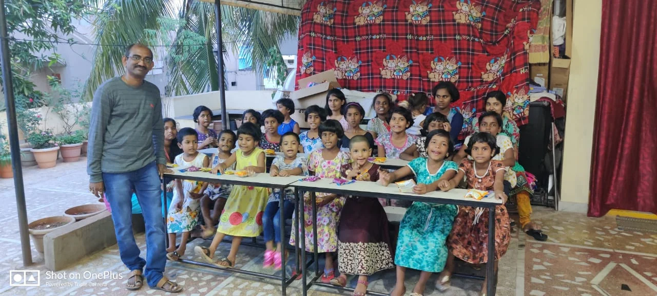 Children gathered around tables with a Surya Helping Hands volunteer during a community celebration